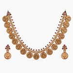 A picture of an Indian artificial gold plated necklace set with a round pendant and matching earrings, featuring intricate filigree work and red gemstones.