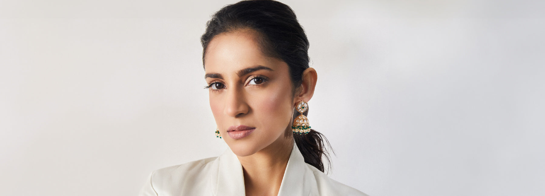 A woman posing while wearing a pair of Indian jhumka earrings, Tarinika is suggesting this as a Women's Day Gift.