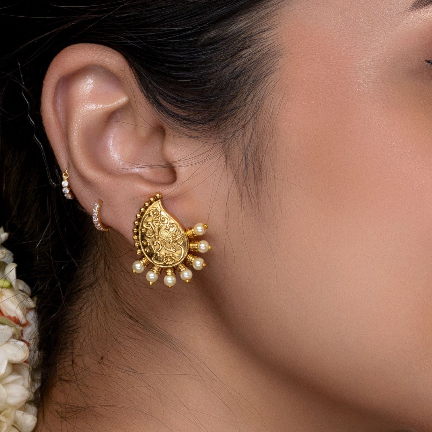 A close up image of a mango shaped gold plated earrings with white beads.