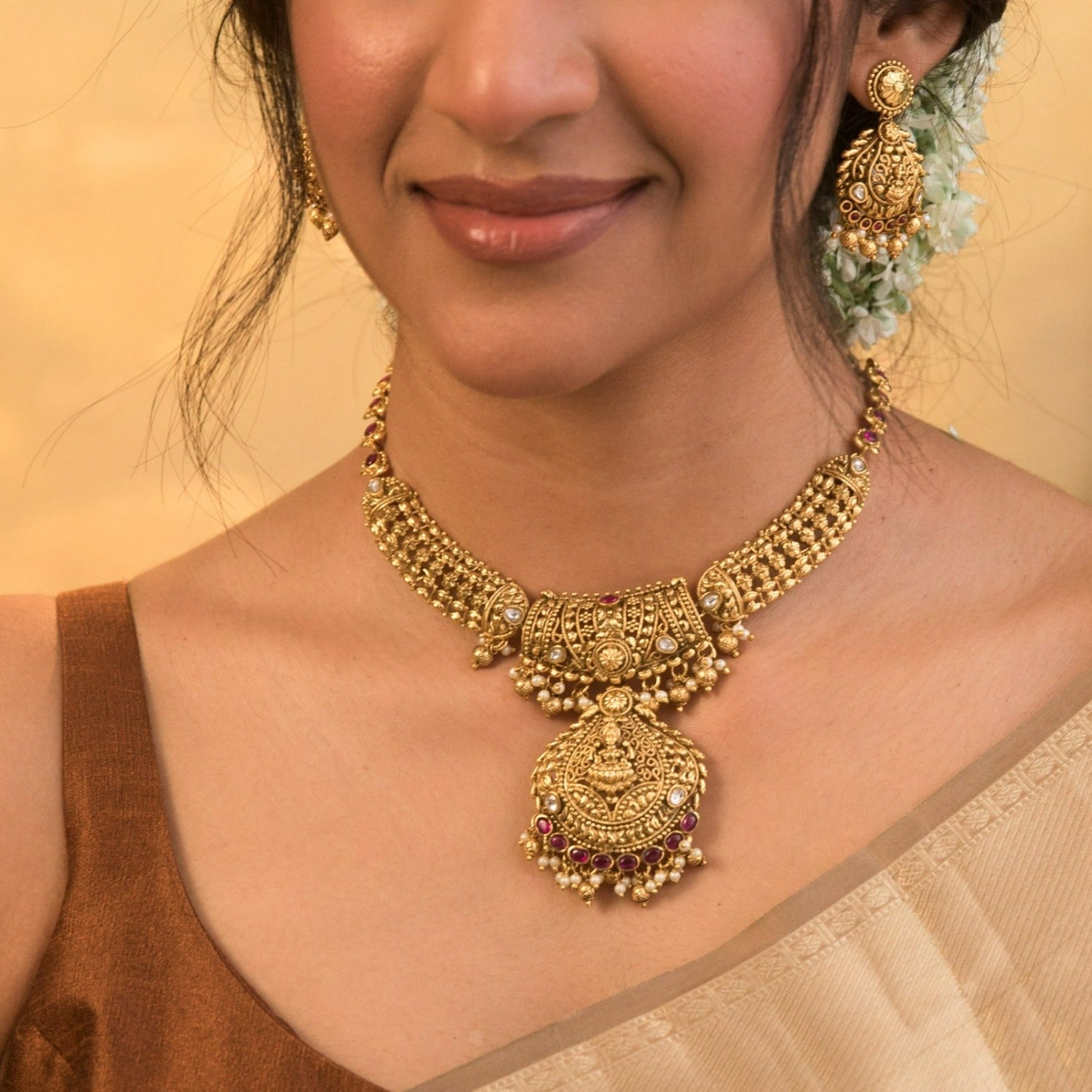 A picture of an Indian artificial gold plated necklace set with a pendant featuring Lakshmi design and red gemstones with matching earrings.