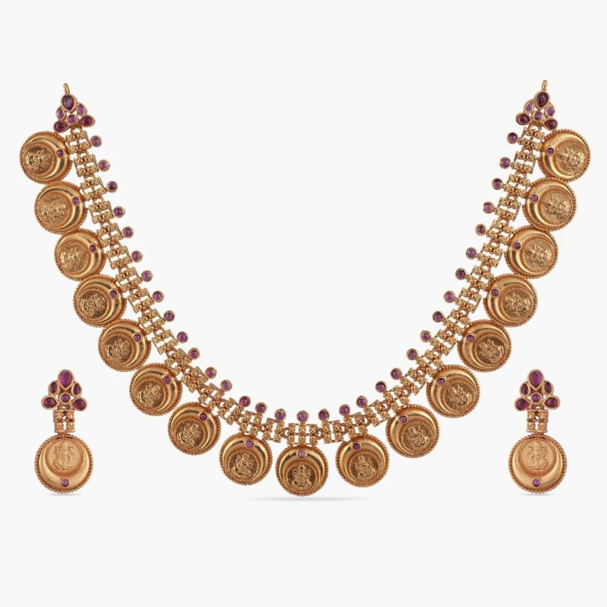 A picture of an Indian artificial gold plated necklace set with a round pendant and matching earrings, featuring intricate filigree work and red gemstones.