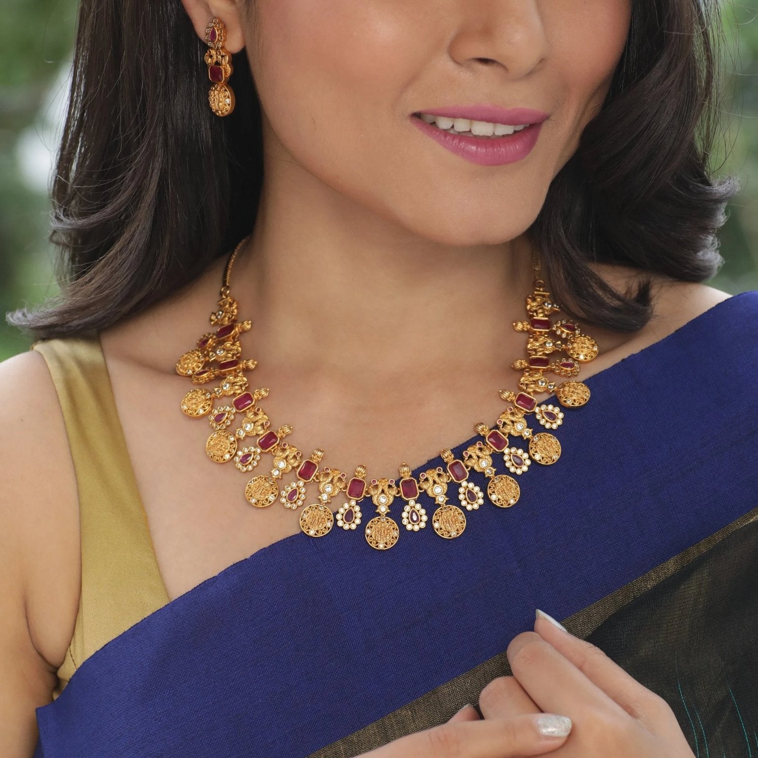 A picture of an Indian artificial necklace and earring set. The set is gold-toned with floral designs and green gemstones.
