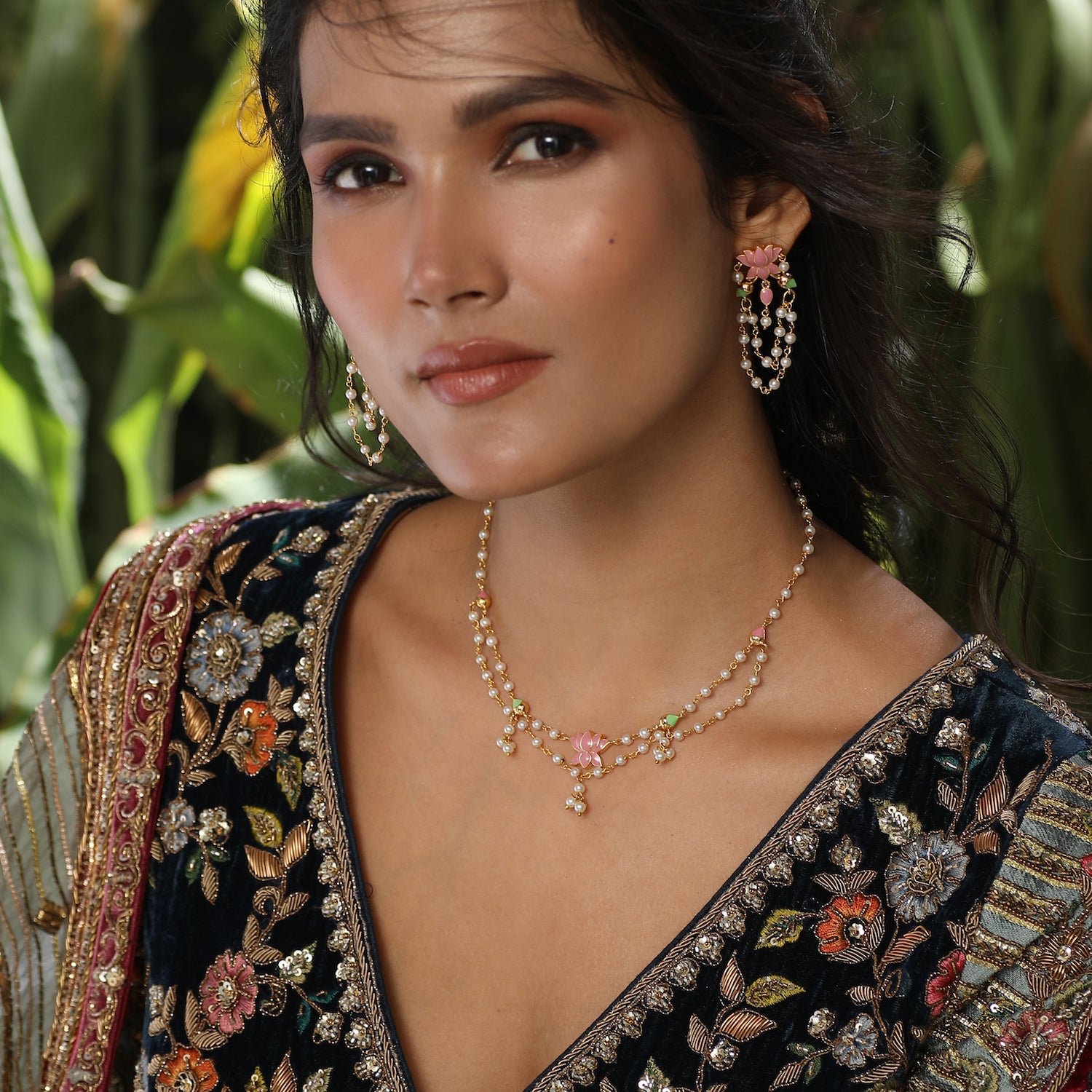 A picture of an Indian artificial layered necklace set with lotus pendant and a gold-toned chain. The earrings are stud style with matching white stones.