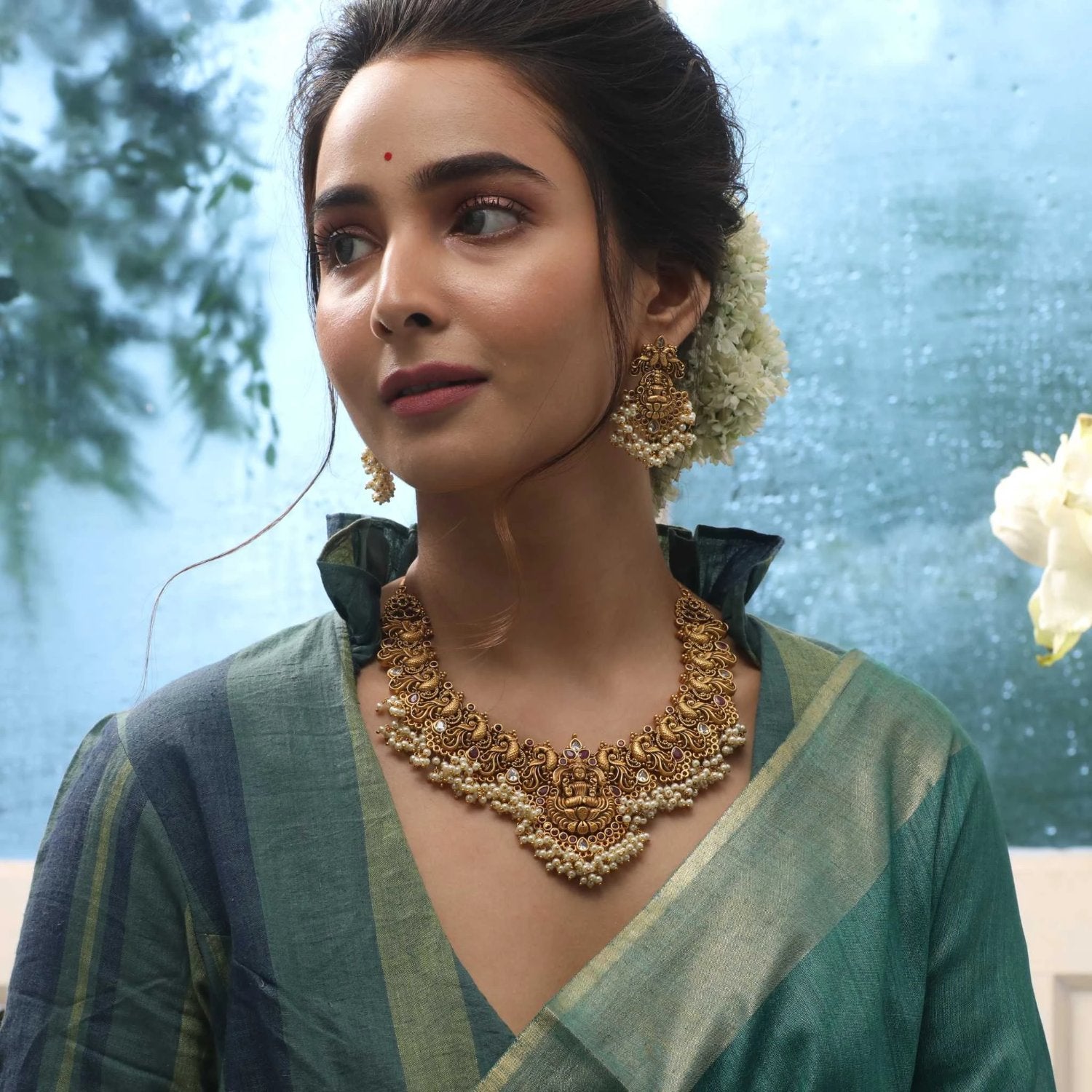 A picture of an Indian artificial gold necklace and earring set. The necklace is embellished with pearls and the earrings are chandelier style.